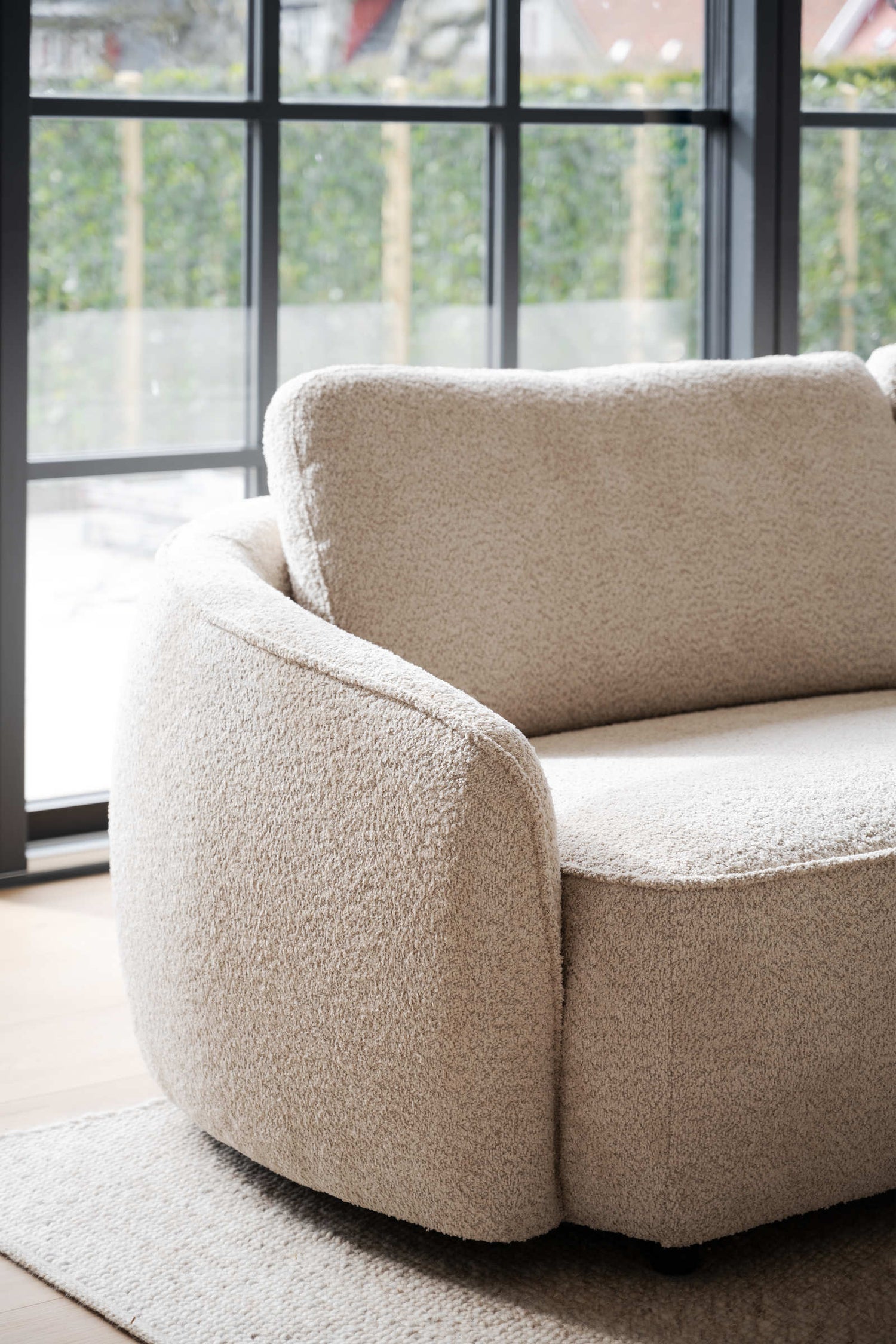 Lähikuvassa Norris-divaanisohvan kaarevaa muotoilua. Verhoiluna vaalea beige Anna 2-kangas ja sohvassa on mustat muovijalat.