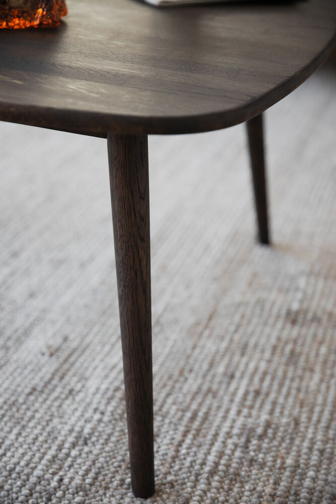 Lähikuvassa neliön Tompkins-sohvapöydän ruskeaa tammikantta ja jalkoja.