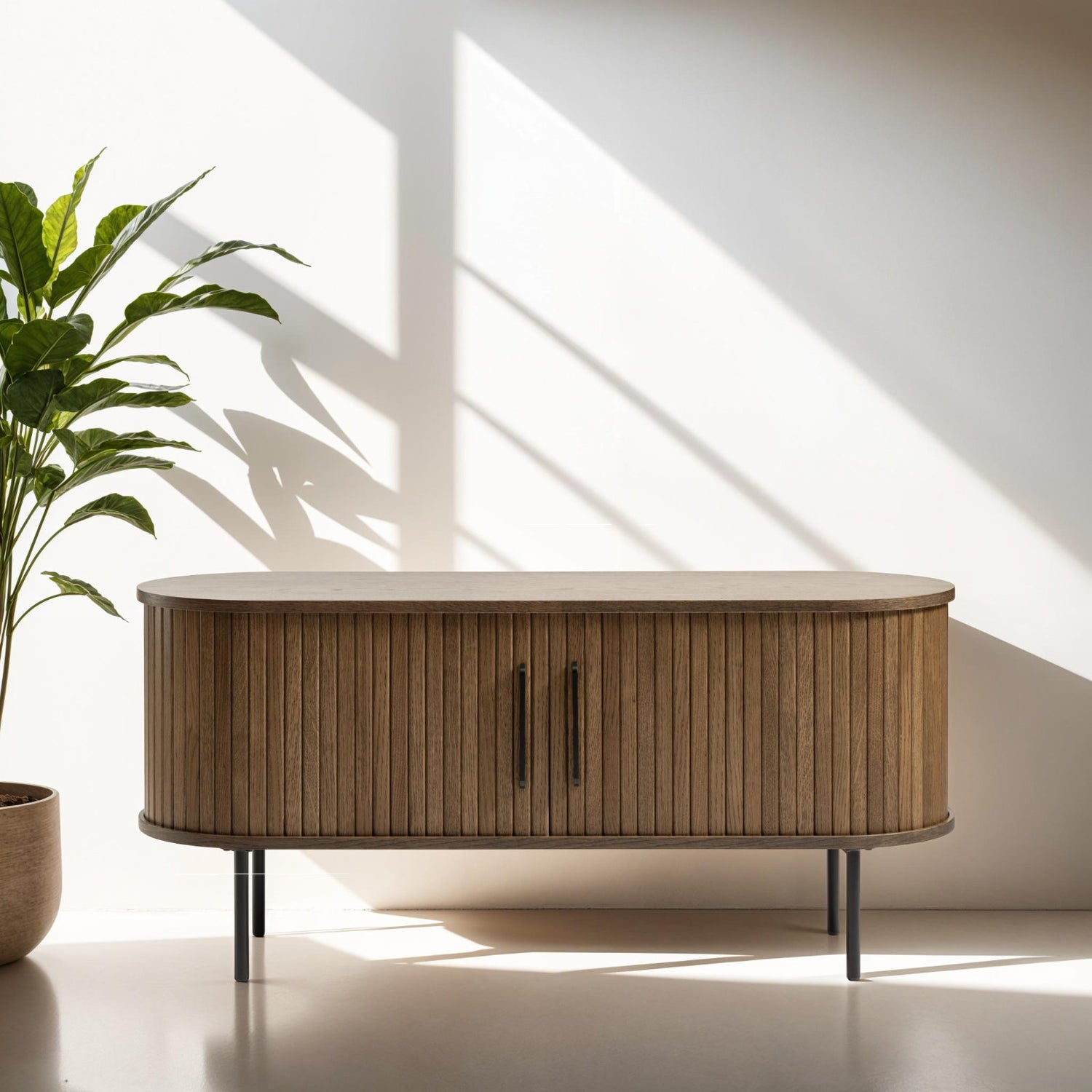 Kuvassa on ovaalinmuotoinen Nola-tv-taso 120 cm, savutammenvärinen. Tasossa on mustat metalliset vetimet liukuovissa ja mustat säädettävät metallijalat.