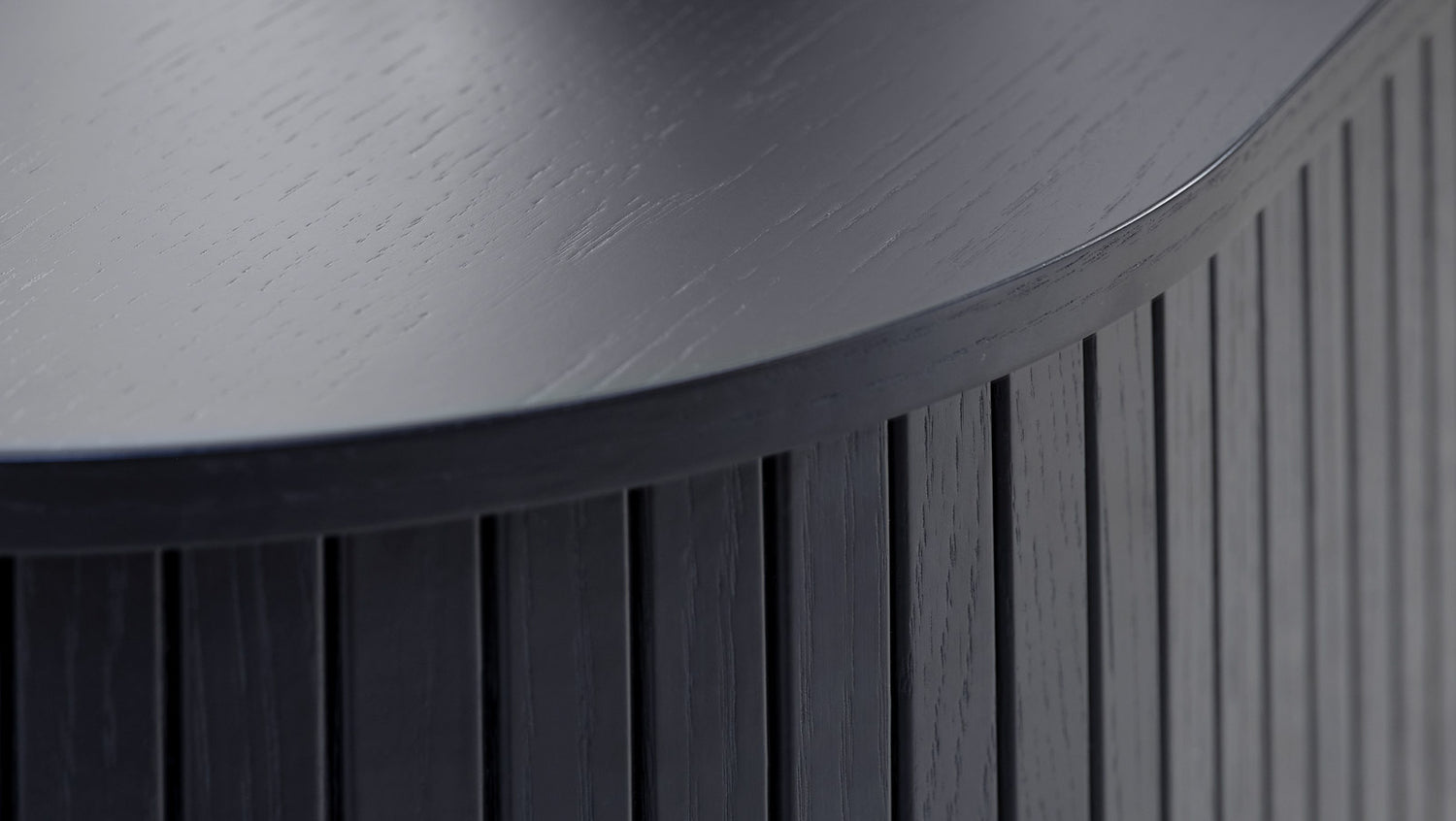 Lähikuvassa ovaalinmuotoisen Nola-sohvapöydän mustaa kannen pintaa ja paneelipäällysteisiä liukuovia.