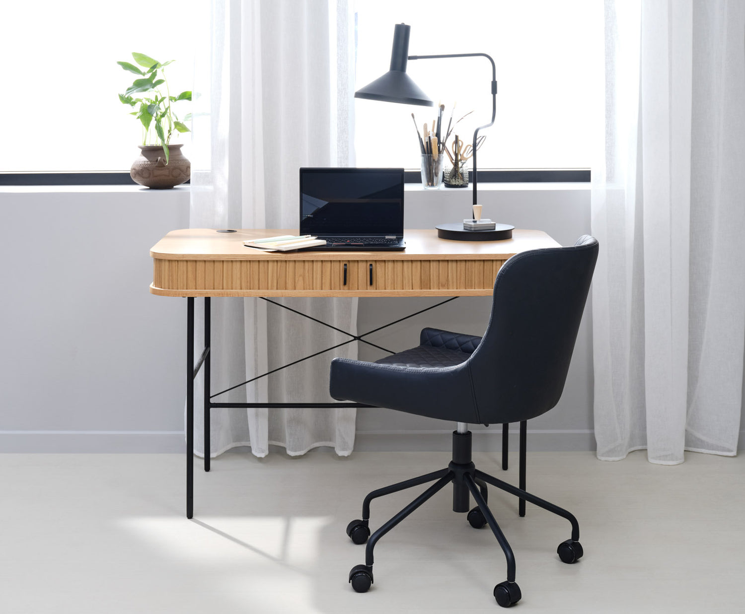 Kuvassa on Nola-työpöytä tammenvärisenä. Sormipaneloiduissa liukuovissa on mustat metalliset vetimet ja metallijalat ovat mustat.