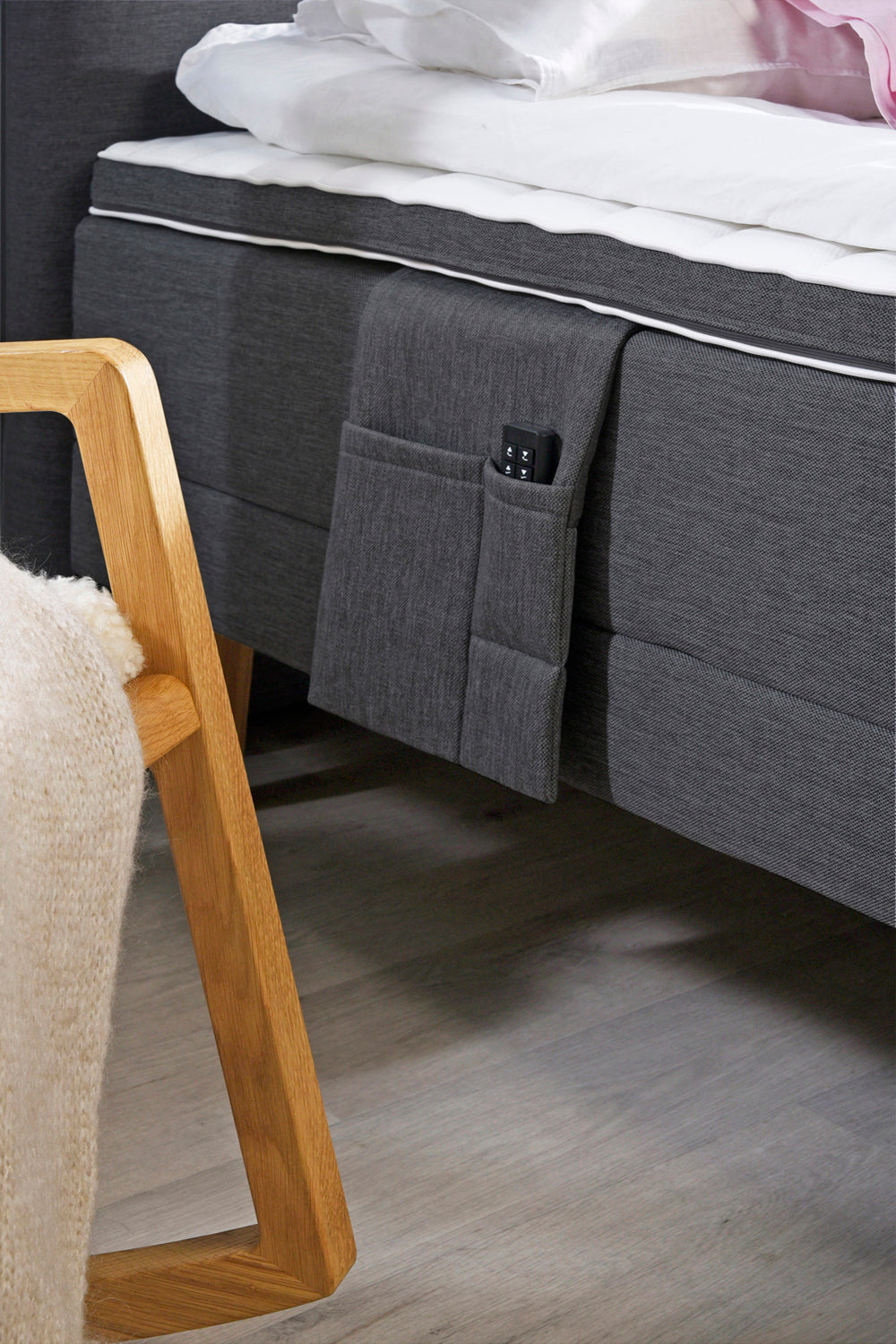 Lähikuvassa antrasiitin värisen Aava-moottorisängyn lisävarusteena saatava tarviketasku. Profiloidussa sijauspatjassa on rungon värinen reunus.