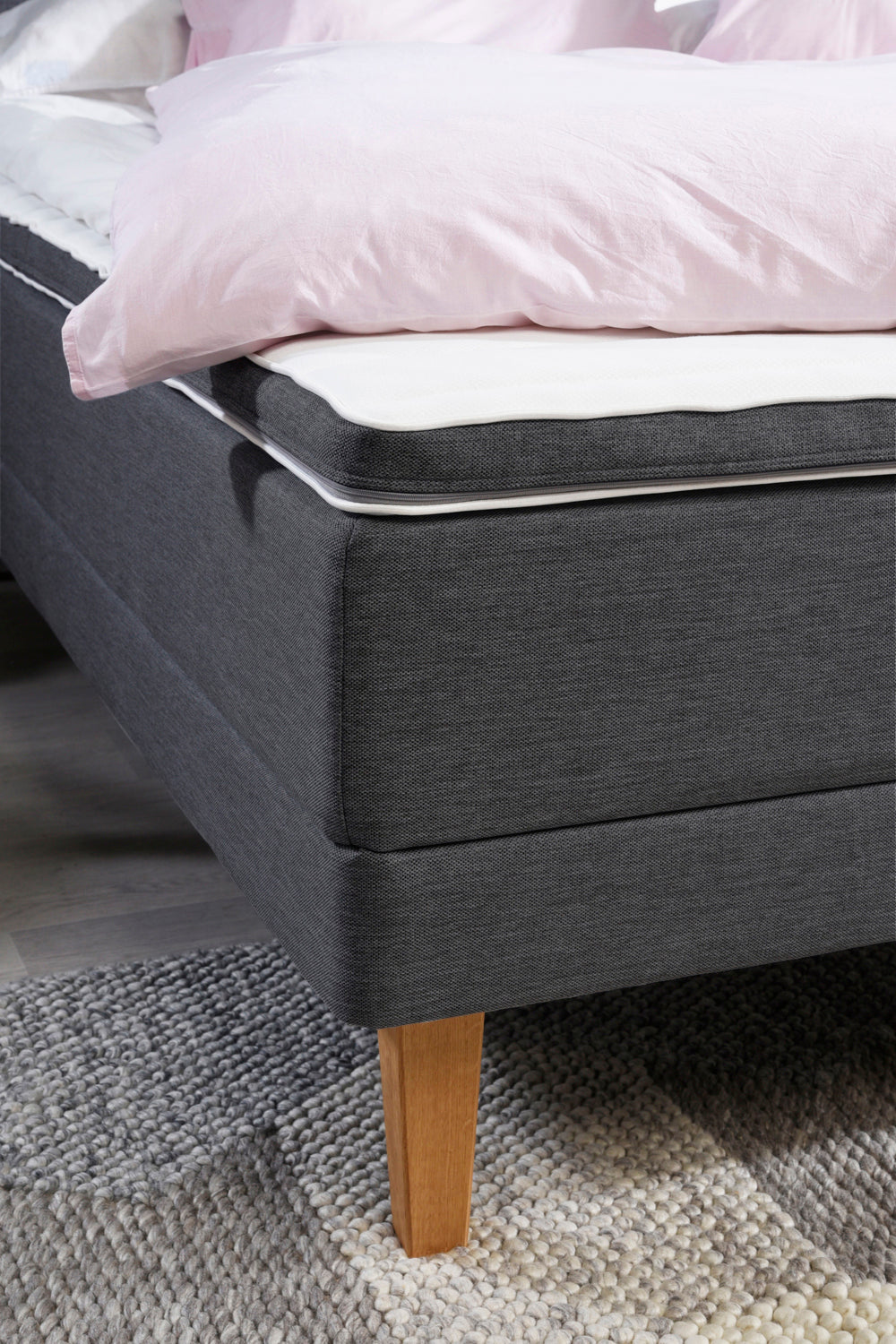 Lähikuvassa antrasiitin värisen Aava-moottorisängyn kulma. Antrasiitin värisessä sängyssä on luonnonväriset Royal-tammijalat ja profiloitu sijauspatja rungon värisellä reunuksella.