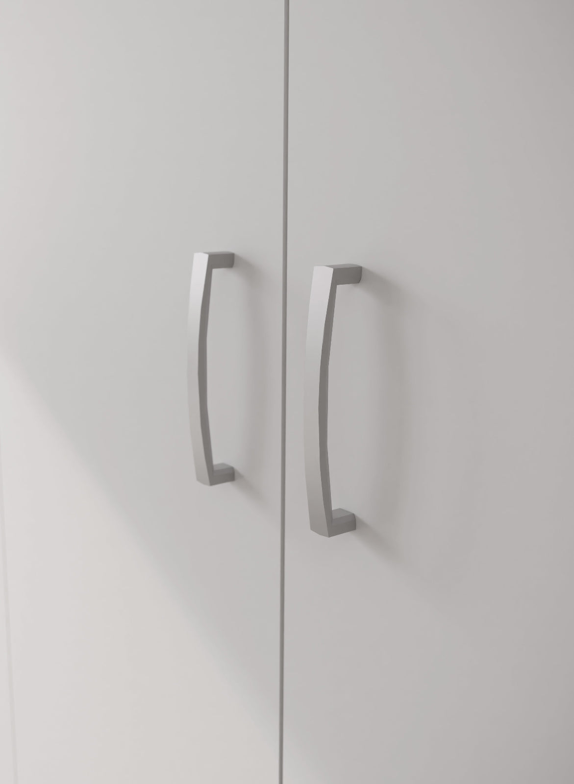 Lähikuvassa kokovalkoisen 3-ovisen Kira-komeron tuplaovikaapin hopeanharmaat vetimet.