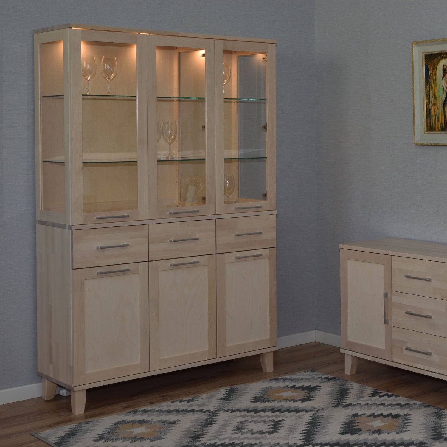 Kuvassa on valkolakattu Vuokatti-vitriini. Vitriinissä on lasikaapisto lasihyllyillä, alaosan tilava senkki kaappien peiliovilla, sekä pitkänmalliset RST-vetimet. Lasikaapin sisällä olevat valot/viinilasit eivät kuulu senkin hintaan.