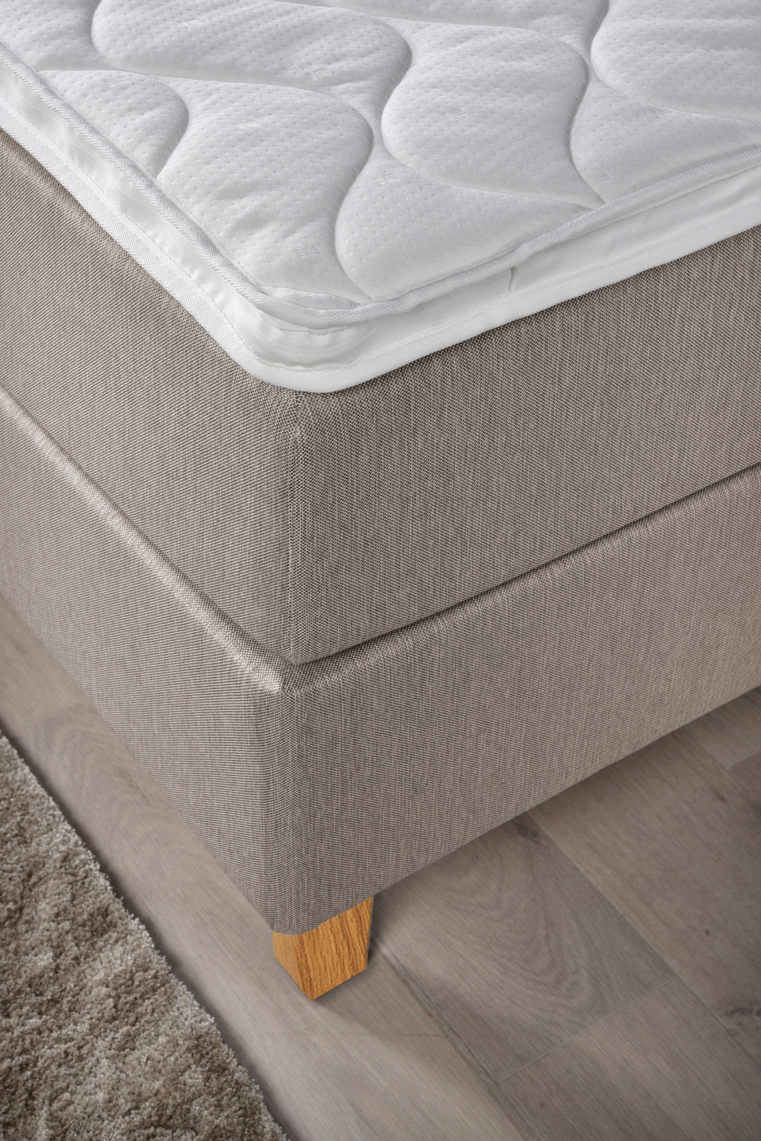Yksityiskohta Ranta-jenkkisängystä. Kuvassa on beigenvärinen Ranta-jenkkisänky luonnonvärisillä Royal-tammijaloilla ja valkoisella profiloidulla sijauspatjalla.