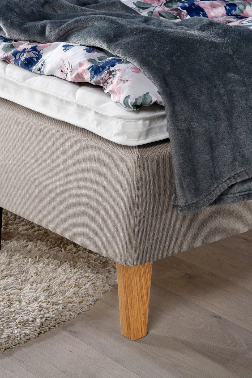 Yksityiskohta Ranta-runkopatjasta. Kuvassa on beige sänky luonnonvärisillä Royal-tammijaloilla ja valkoisella profiloidulla sijauspatjalla.