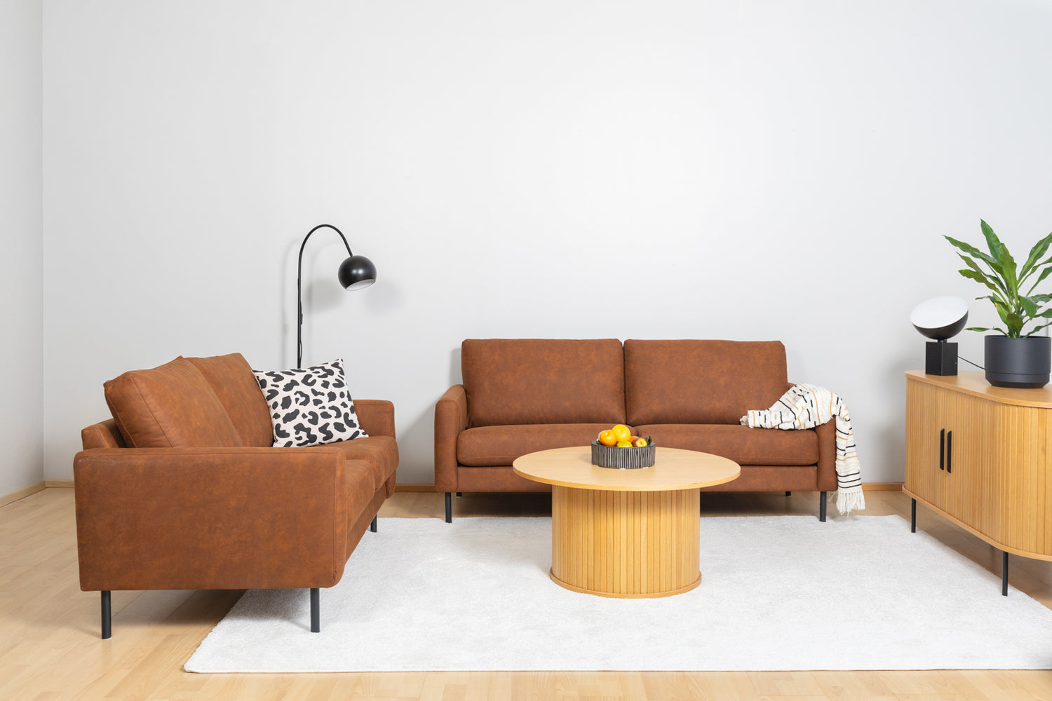 Kuvassa etualalla on Nola-sohvapöytä luonnonvärisenä ja oikealla Nola-senkki. Sohvat ovat Mila 2- ja 3-istuttavat Texas-kankaisena. Mattokympin Louna-matto kokoaa sohvakaluston yhteen.