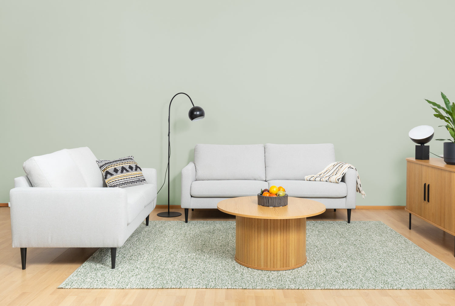 Kuvassa Mattikympin vihreä Anna-villamatto kokoaa olohuoneen kalusteet yhteen: 2-ja 3-istuttavat Mila-sohvat hiekanvärisellä Coria 02 -kankaalla ja wengen värisillä pyöreäkartionjaloilla. Sohvan edessä on Nola-sohvapöytä ja sivulla Nola-senkki 140 cm. Sohvilla on lisäksi Mattokympin Hulda-koristetyyny ja Sävel Raita-torkkupeitto. Valaisimet ovat Pod-pöytä- ja Round Single -lattiavalaisin.