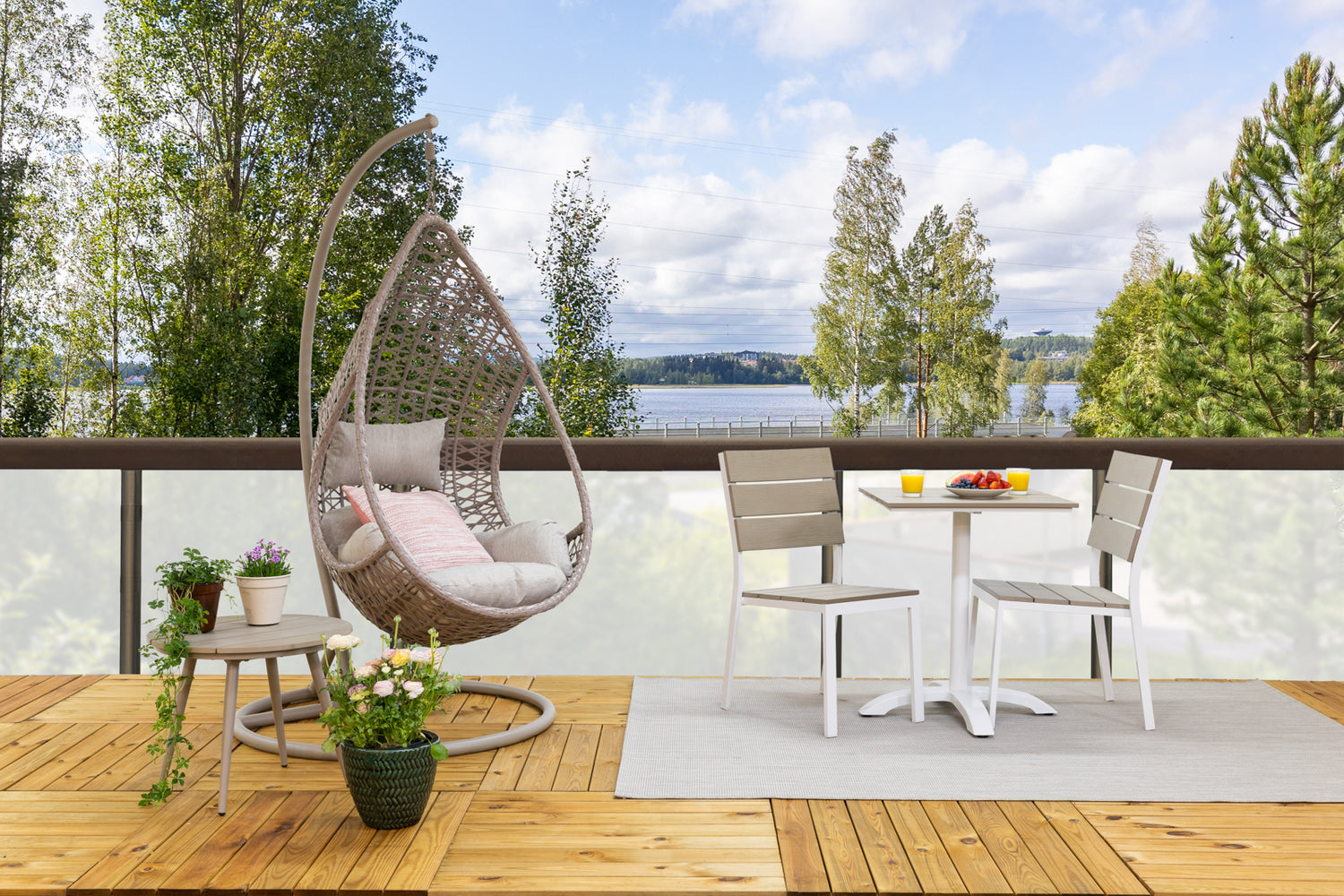 Kuvassa on beige Suvi-riippukeinu ja Suvi Cafe-parvekepöytä Suvi Aintwood-tuoleineen kahdelle. Keinun vasemmalla puolella on beige Suvi-sohvapöytä. Kuvassa lisäksi Mattokympin pellavanvärinen Pilke-matto.