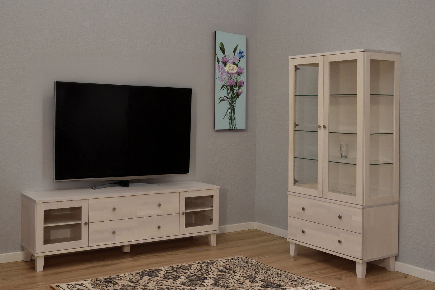 Kuvassa on valkolakattu Vuokatti-vitriini. Vitriinissä on lasikaappi lasihyllyillä, alaosan isot laatikot, sekä nikkelinväriset D-26-nuppivetimet. Lisäksi kuvassa on Vuokatti-sarjan tv-taso 14/5.