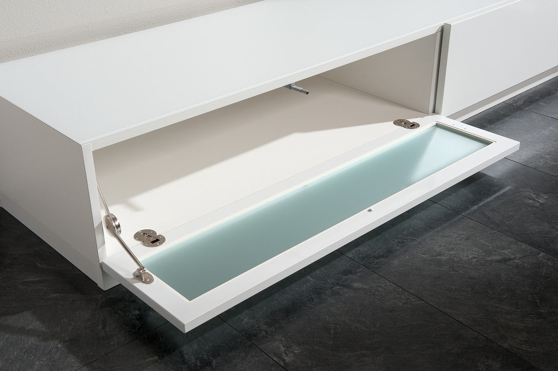 Hohtavan valkoiset Lumo-sarjan kalusteet toimivat ilman vetimiä, push to open -mekanismilla. Tv-tasossa on lasinen klaffiovi ja laatikko.