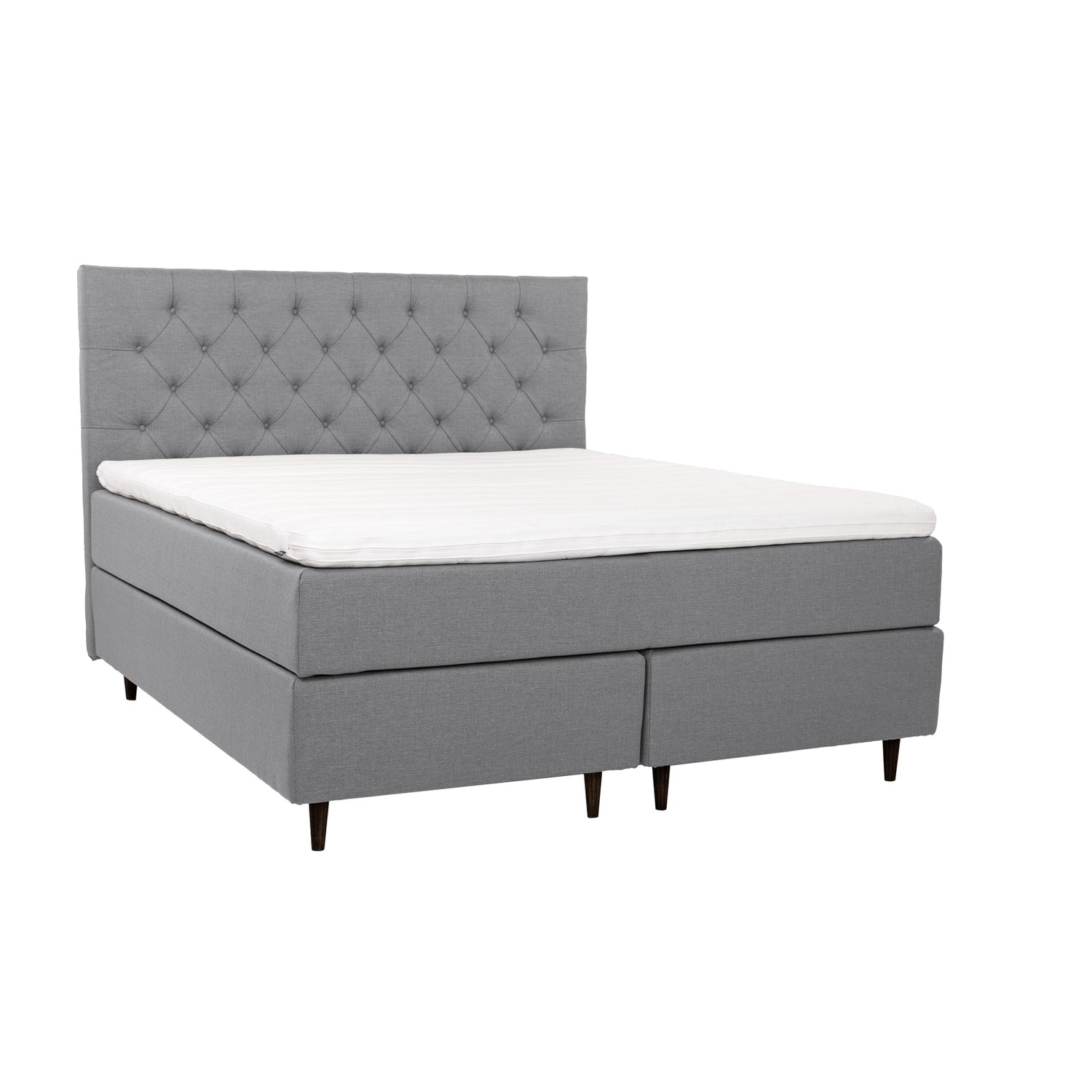 Harmaa Hilding Cross -jenkkisänky tummanruskeilla pyöreillä Hilding Raita -tammijaloilla ja yhtenäisellä Ergo -sijauspatjalla. Kuvan Cross -sängynpääty myydään erikseen.