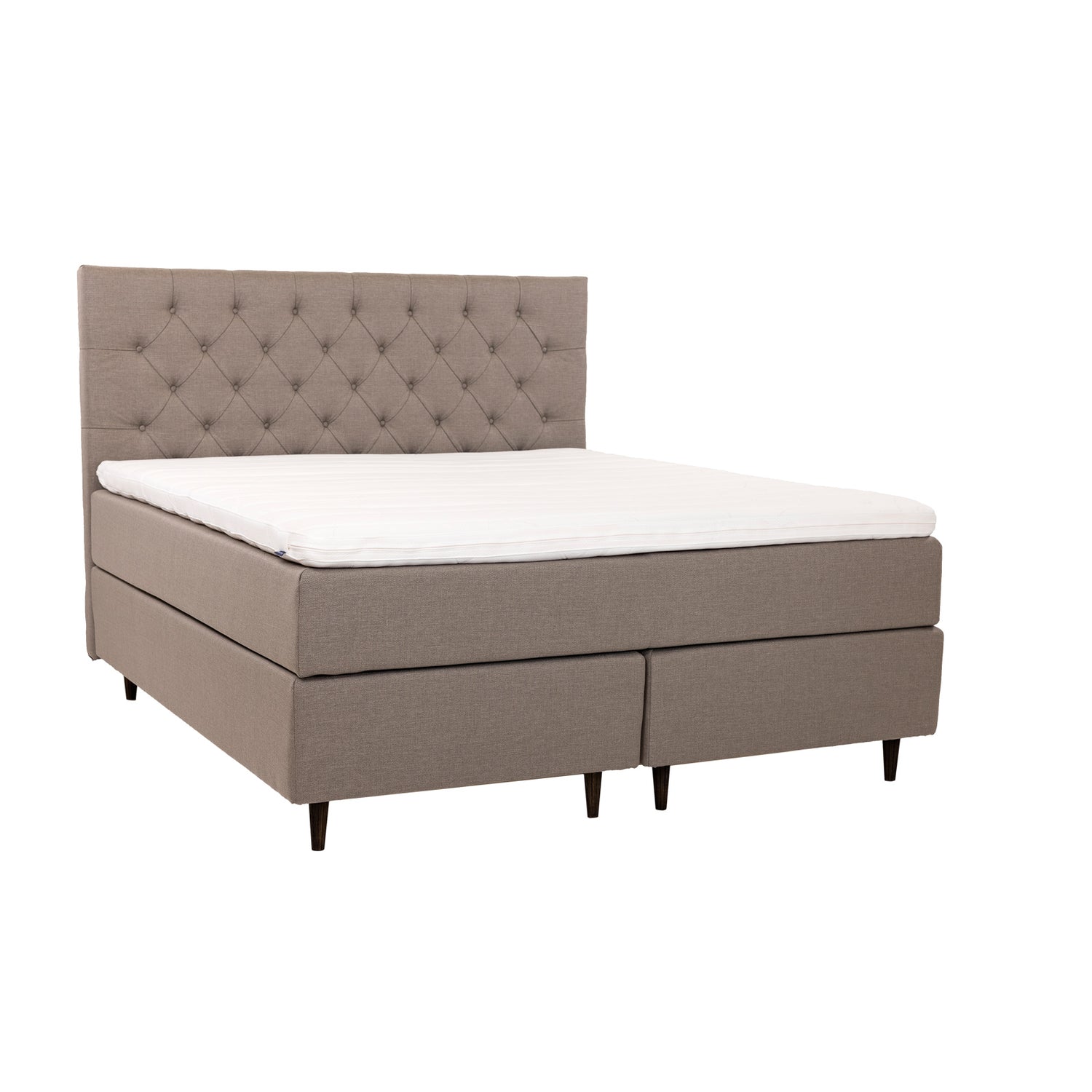 Hiekanvärinen Hilding Cross -jenkkisänky tummanruskeilla pyöreillä Hilding Raita -tammijaloilla ja yhtenäisellä Ergo -sijauspatjalla. Kuvan Cross -sängynpääty myydään erikseen.