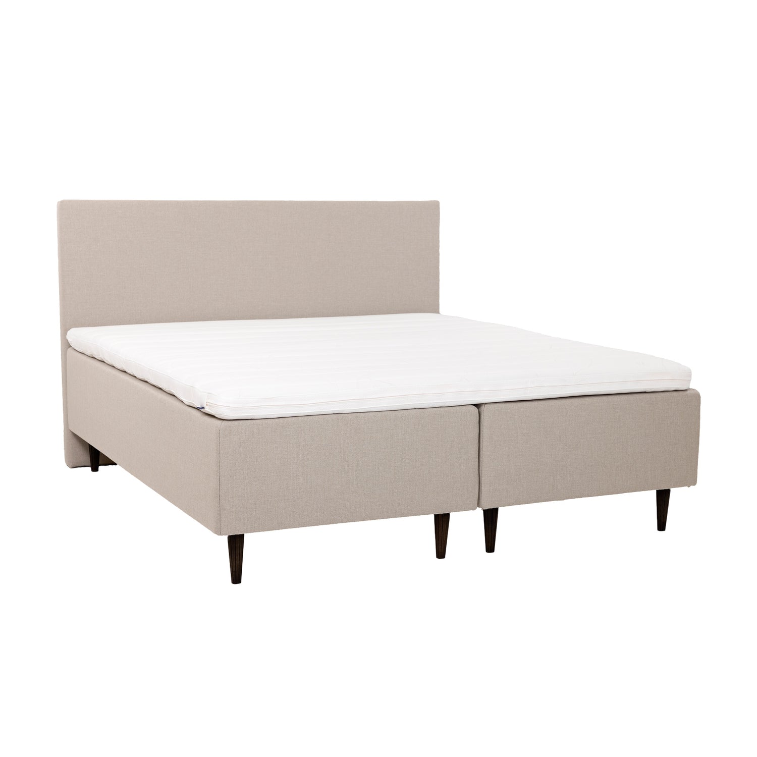 Beiget Hilding Cross -runkopatjat 90 x 200 cm tummanruskeilla 23 cm korkeilla Hilding Raita -tammijaloilla ja yhtenäisellä Hilding Ergo -sijauspatjalla. Kuvan Original -sängynpääty myydään erikseen.