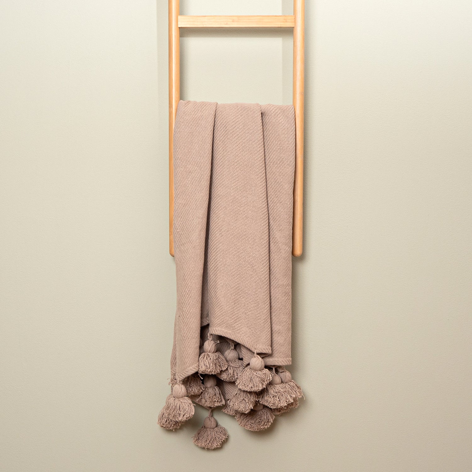 Sävel Tupsu-torkkupeitto beigen värisenä - peiton päädyissä on tupsut.