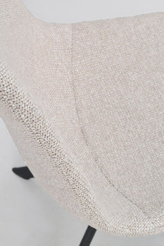 Lähikuvassa Dunmore-tuolin vaalean beigeä kangasverhoilua ja mustat alaspäin levittyvät metallijalat.