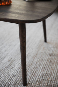 Lähikuvassa neliön Tompkins-sohvapöydän ruskeaa tammikantta ja jalkoja.