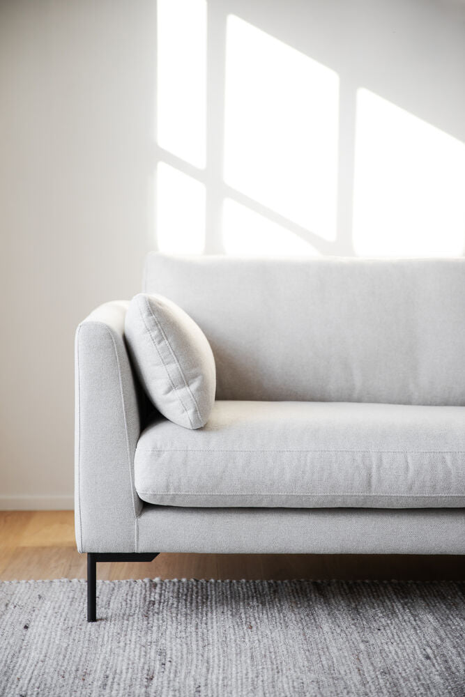Lähikuvassa 2-3-istuttava Corwin-sohva vaalealla Rita 1-kankaalla verhoiltuna ja mustilla metallijaloilla.