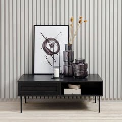 Kuvassa Pensacola-sohvapöytä, musta. Sohvapöydän molemminpuolisten laatikoiden etulevyissä on yksityiskohtana polyrottinki. Mustat metallijalat.