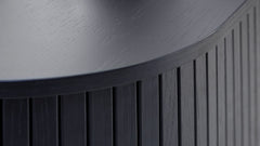 Lähikuvassa ovaalinmuotoisen Nola-sohvapöydän mustaa kannen pintaa ja paneelipäällysteisiä liukuovia.