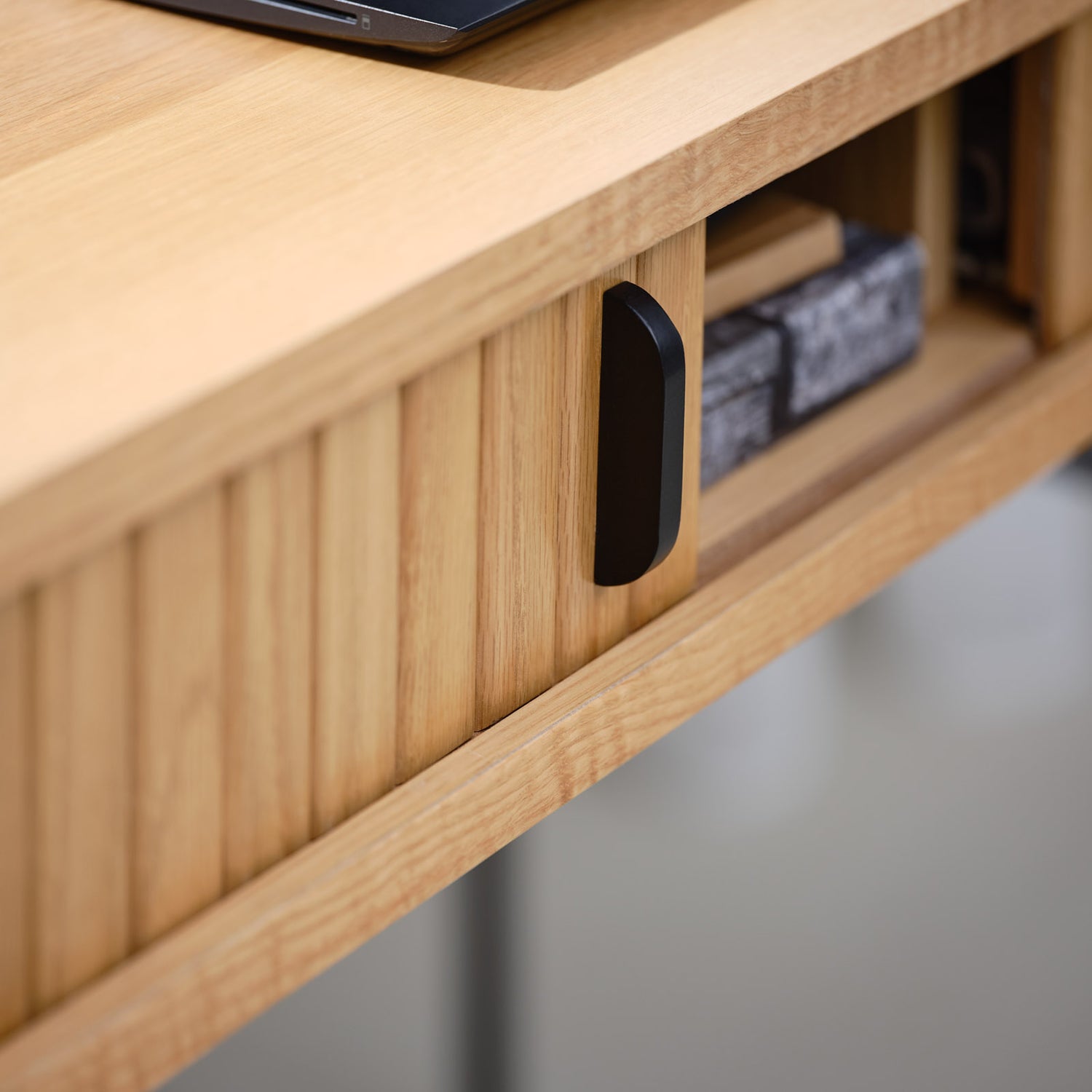 Lähikuvassa Nola-työpöytä tammenvärisenä. Sormipaneloiduissa liukuovissa on mustat metalliset vetimet ja metallijalat ovat mustat.