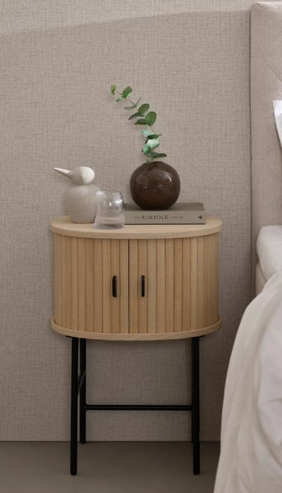 Kuvassa on Nola-yöpöytä tammenvärisenä. Tasossa on mustat metalliset vetimet ja säädettävät metallijalat ovat mustat.