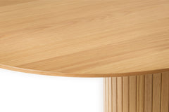 Lähikuvassa luonnonvärisen Nola-ruokapöydän kansilevyä ja jykevää jalkaa, johon panelointi on tuomassa ilmettä.