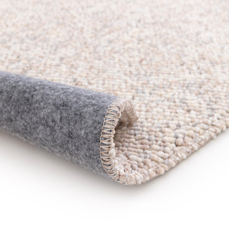 Lähikuvassa on beige-harmaa sileäpintainen Ahto-matto. Matto on raullattuna ja näkyvissä on myös sen pohjausta.