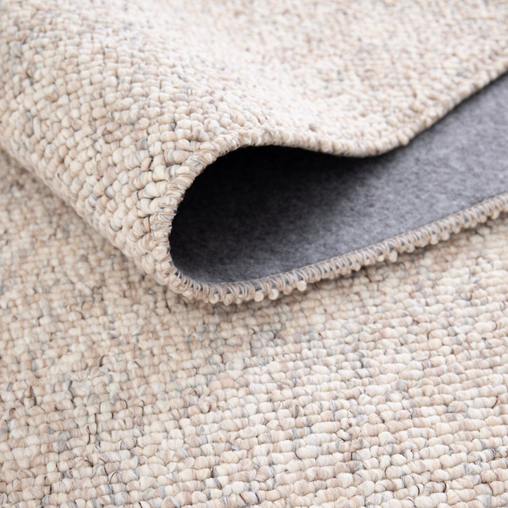 Lähikuvassa on beige-harmaa sileäpintainen Ahto-matto. Matto on taitettuna ja näkyvissä on myös sen pohjausta.