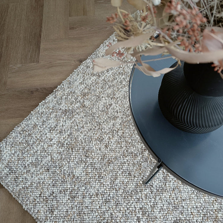 Kuvassa on beige-harmaa sileäpintainen Ahto-matto kuvattuna sohvapöydän alla.