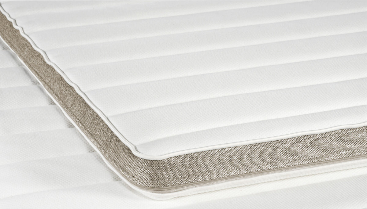 Profiloidun Havu-sijauspatjan reunassa on sängyn rungon värinen hiekanvärinen boordi. Petauspatjan makuupinnoilla on valkoinen joustoneulos.