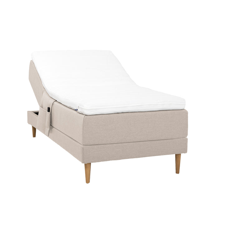 Beigenvärinen Hilding Cross -moottorisänky tammenvärisillä Hilding Raita -tammijaloilla, Hilding Ergo -sijauspatjalla ja Hilding -tarviketaskulla.