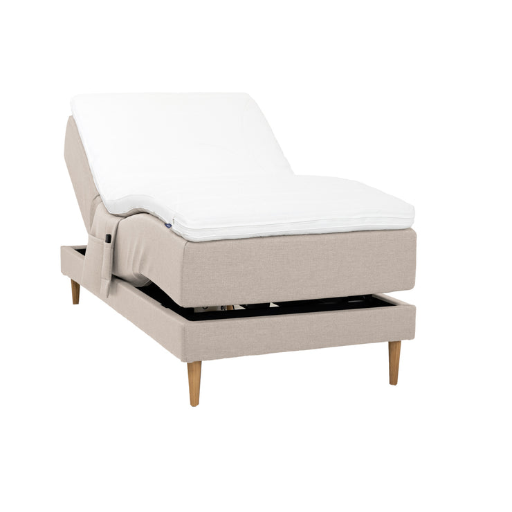 Beigenvärinen Hilding Cross -moottorisänky tammenvärisillä Hilding Raita -tammijaloilla, Hilding Ergo -sijauspatjalla ja Hilding -tarviketaskulla.