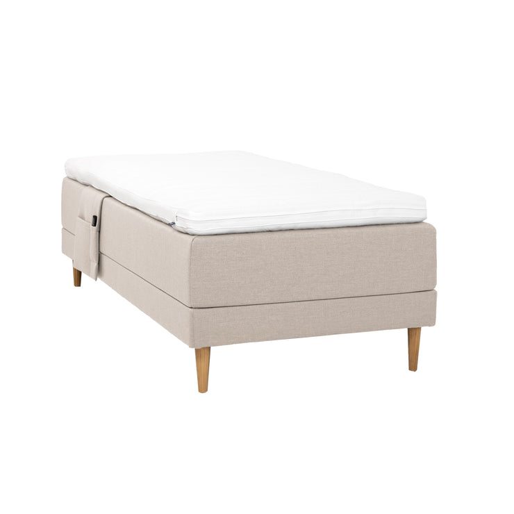 Beigenvärinen Hilding Cross -moottorisänky tammenvärisillä Hilding Raita -tammijaloilla, Hilding Ergo -sijauspatjalla ja Hilding -tarviketaskulla.