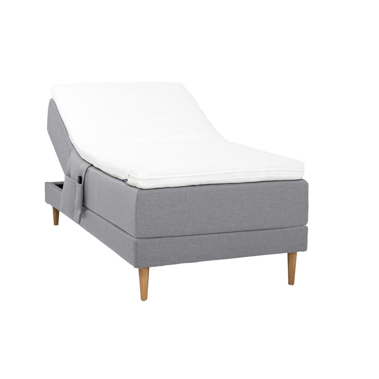 Harmaa Hilding Cross -moottorisänky tammenvärisillä Hilding Raita -tammijaloilla, Hilding Ergo -sijauspatjalla ja Hilding -tarviketaskulla.