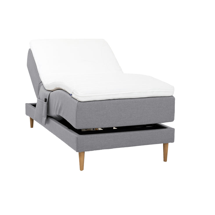 Harmaa Hilding Cross -moottorisänky tammenvärisillä Hilding Raita -tammijaloilla, Hilding Ergo -sijauspatjalla ja Hilding -tarviketaskulla.