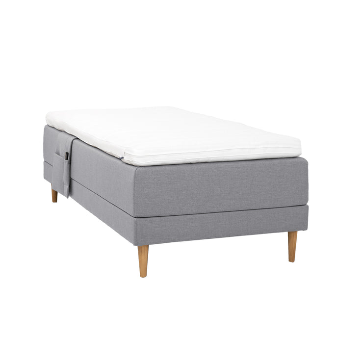 Harmaa Hilding Cross -moottorisänky tammenvärisillä Hilding Raita -tammijaloilla, Hilding Ergo -sijauspatjalla ja Hilding -tarviketaskulla.