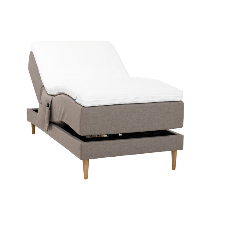 Hiekanvärinen Hilding Cross -moottorisänky tammenvärisillä Hilding Raita -tammijaloilla, Hilding Ergo -sijauspatjalla ja Hilding -tarviketaskulla.