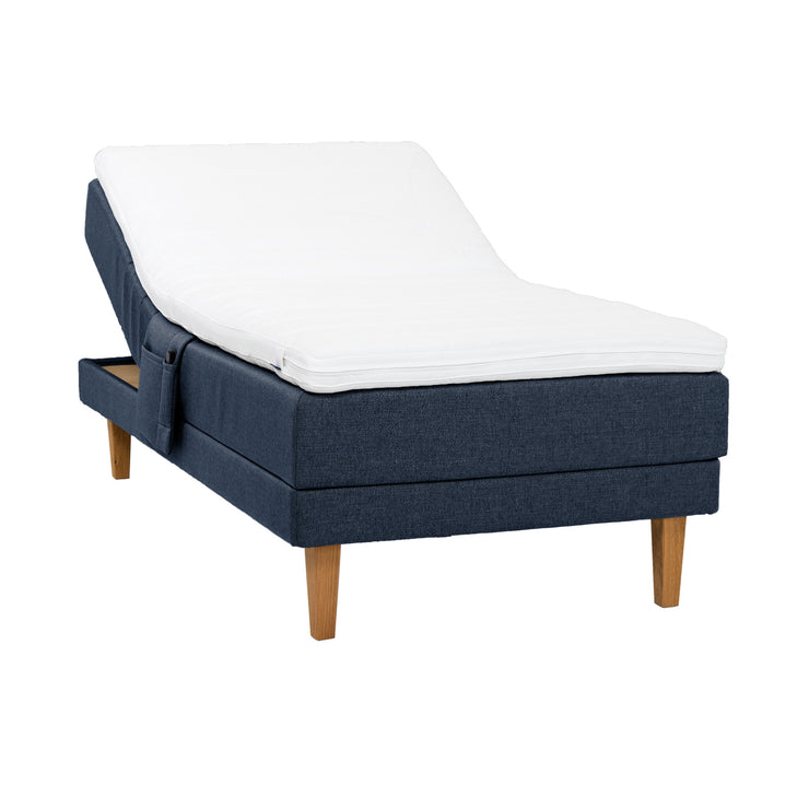 Sininen Hilding Feel -moottorisänky 120 x 200 cm luonnonvärisillä 23 cm korkeilla Royal -tammijaloilla ja Hilding Hybrix Air Coolmax -sijauspatjalla. Kuvan tarviketasku myydään erikseen.