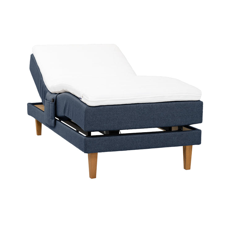 Sininen Hilding Feel -moottorisänky 120 x 200 cm luonnonvärisillä 23 cm korkeilla Royal -tammijaloilla ja Hilding Hybrix Air Coolmax -sijauspatjalla. Kuvan tarviketasku myydään erikseen.