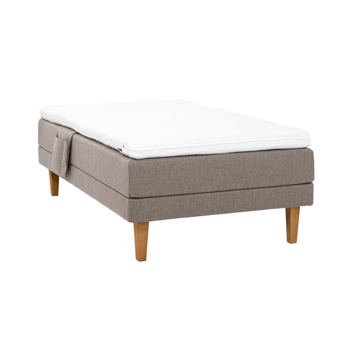 Hiekanvärinen Hilding Feel -moottorisänky 120 x 200 cm luonnonvärisillä 23 cm korkeilla Royal -tammijaloilla ja Hilding Hybrix Air Coolmax -sijauspatjalla. Kuvan tarviketasku myydään erikseen.