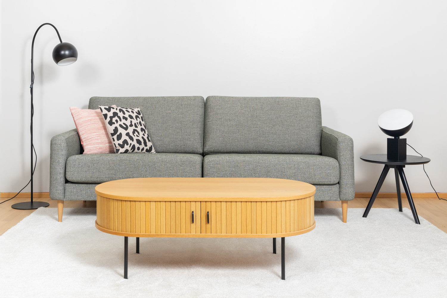 Kuvassa on oikealla musta Pod-poytavalaisin  mustan Yumi-sarjapöydän päällä ja vasemmalla Round Single -lattiavalaisin. Lisäksi kuvassa on Ilona 3h-sohva, Nola-sohvapöytä, valkoinen Louna-matto, sekä koristetyynyt Rita ja Kesalahti.