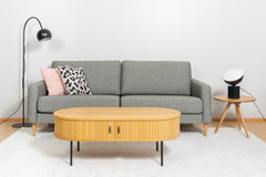 Kuvassa edessä on Nola-sohvapöytä luonnonvärisenä. Sohva on Ilona 3-istuttava ja sohvapöytänä Yumi-sarjapöytä. Mattokympin Louna-matto kokoaa sohvakaluston yhteen.