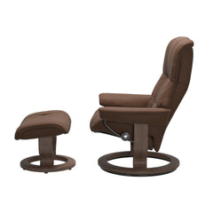Stressless Mayfair M -lepotuoli ja rahi ruskeana: Warm Brown 87 Batick-nahkaverhoilulla ja Walnut 06 -Classic-puujalustalla.