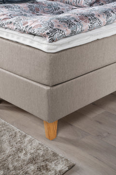 Yksityiskohta Ranta-jenkkisängystä. Kuvassa on beigenvärinen Ranta-jenkkisänky luonnonvärisillä Royal-tammijaloilla ja valkoisella profiloidulla sijauspatjalla.