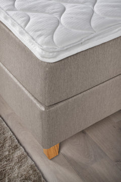 Yksityiskohta Ranta-jenkkisängystä. Kuvassa on beigenvärinen Ranta-jenkkisänky luonnonvärisillä Royal-tammijaloilla ja valkoisella profiloidulla sijauspatjalla.