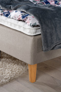 Yksityiskohta Ranta-runkopatjasta. Kuvassa on beige sänky luonnonvärisillä Royal-tammijaloilla ja valkoisella profiloidulla sijauspatjalla.