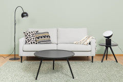 Kuvassa on musta Pod-pöytävalaisin Rowicon Yumi-sarjapöydällä oikealla, sekä vasemmalla musta Round Single-lattiavalaisin. Lisäksi kuvassa on harmaa Mila 3h sohva, vihreä Anna-matto, musta Daisy-sohvapoyta, Hulda ja Rita-koristetyynyt, sekä Sävel Raita-torkkupeitto.