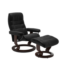 Stressless Opal M -lepotuoli ja rahi mustana: Black 19 Batick-nahkaverhoilulla ja ruskea petsatulla -Classic-puujalustalla.